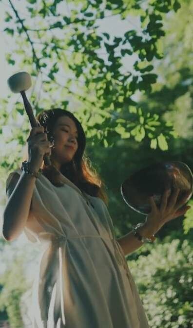 Helen playing a singing bowl beneath green leaves
