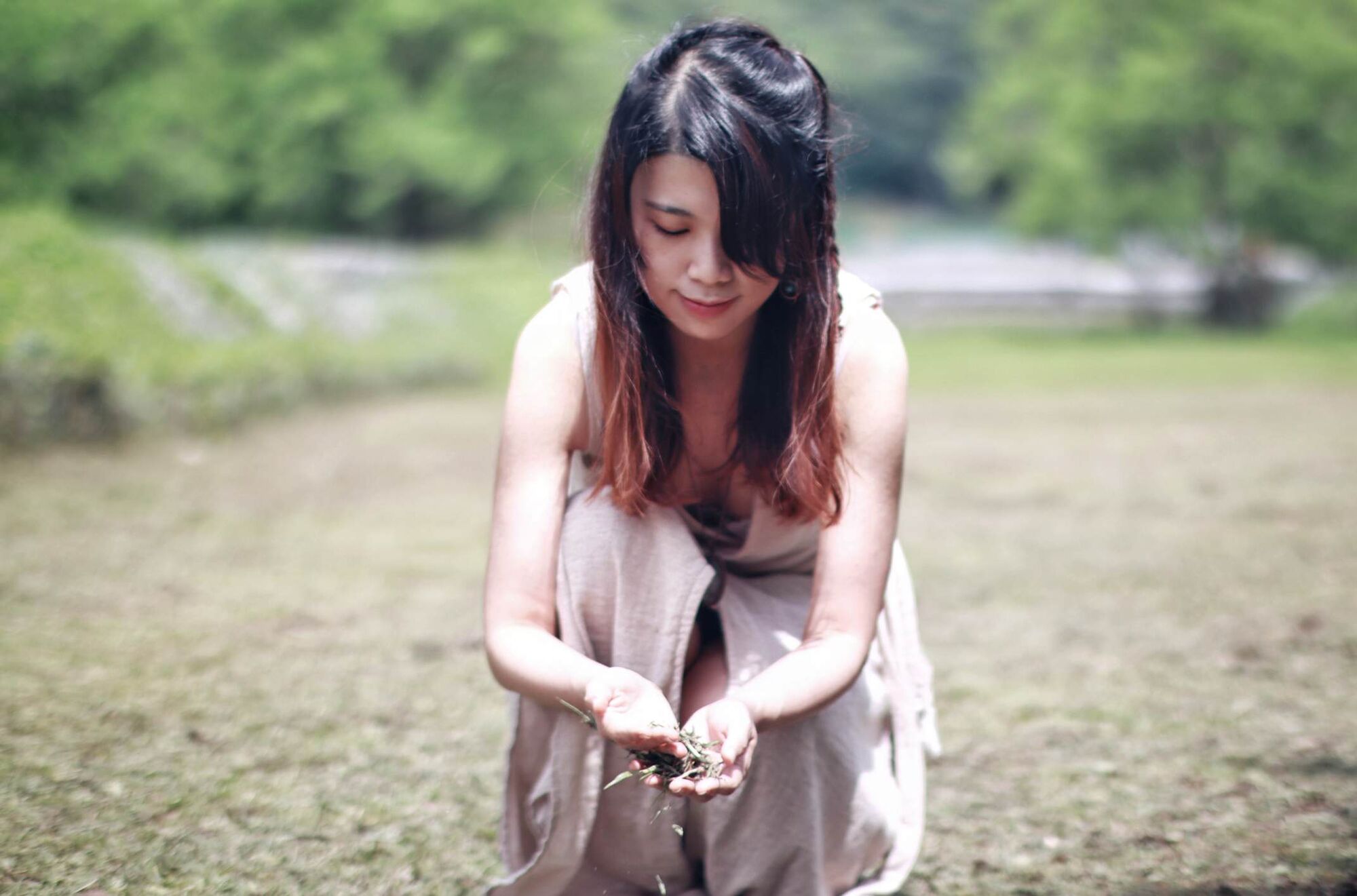 Helen kneeling in a meadow, holding grass in cupped hands